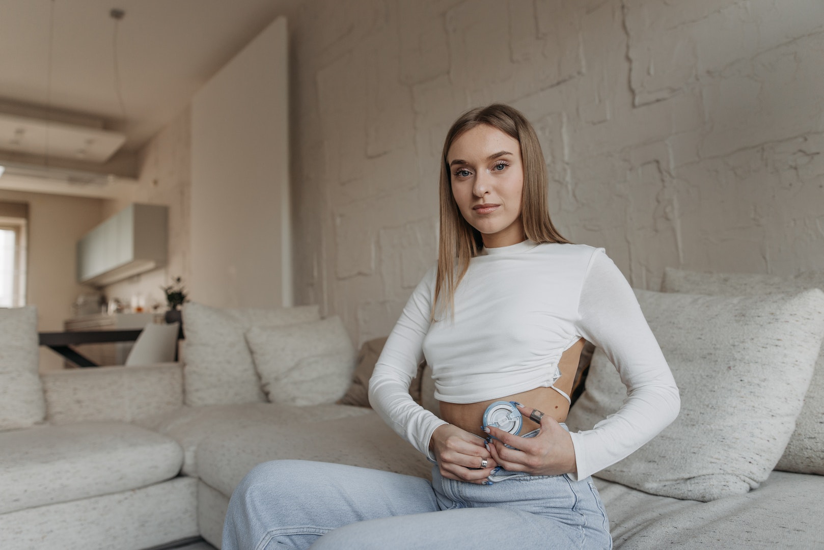Woman in White Long Sleeve Shirt and Blue Denim Jeans Sitting on Gray Couch