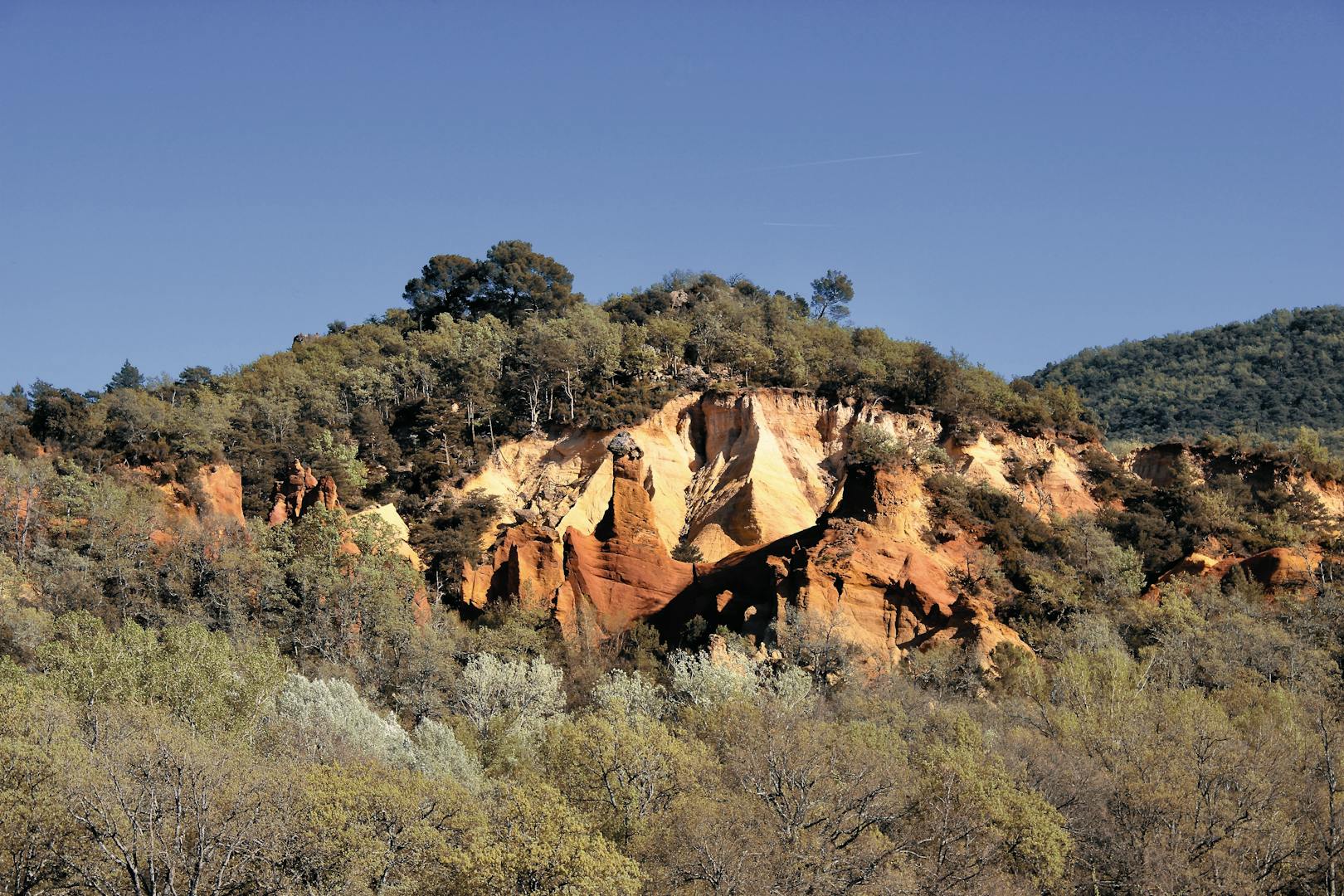 Stunning ochre cliffs surrounded by lush greenery in Rustrel, Provence, France.