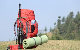 Sac à dos rouge, bâton de marche et tapis de sol posés dans l'herbe au bord d'un sentier