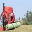 Sac à dos rouge, bâton de marche et tapis de sol posés dans l'herbe au bord d'un sentier