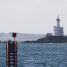 Petit phare blanc à lanterne rouge sur un îlot rocheux, avec au premier plan une balise métallique rouge surmontée d'un voyant carré