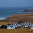 Hameau de maisons blanches aux toits d'ardoise au pied d'une colline couverte de lande, face à une côte rocheuse et à la mer