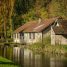 Canal bordé d'arbres aux feuillages d'automne, avec une rive herbeuse et une ancienne maison en pierre au bord de l'eau