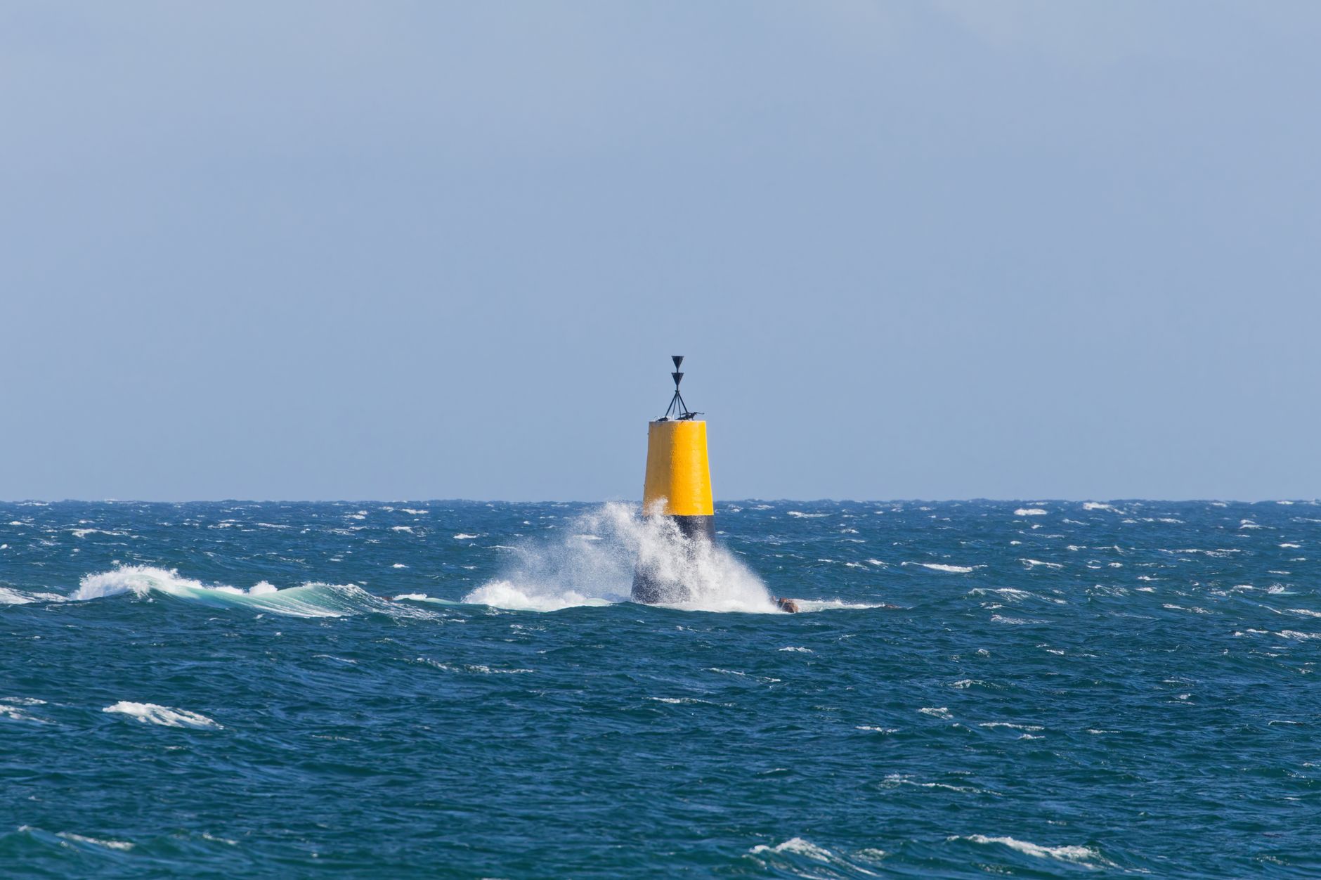 Marque cardinale jaune et noire battue par les vagues, surmontée de deux cônes noirs pointés vers le bas
