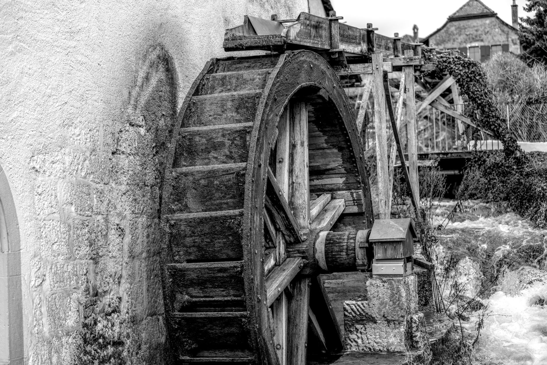 Photo en noir et blanc d'une roue hydraulique verticale en bois contre le mur en pierre d'un ancien moulin